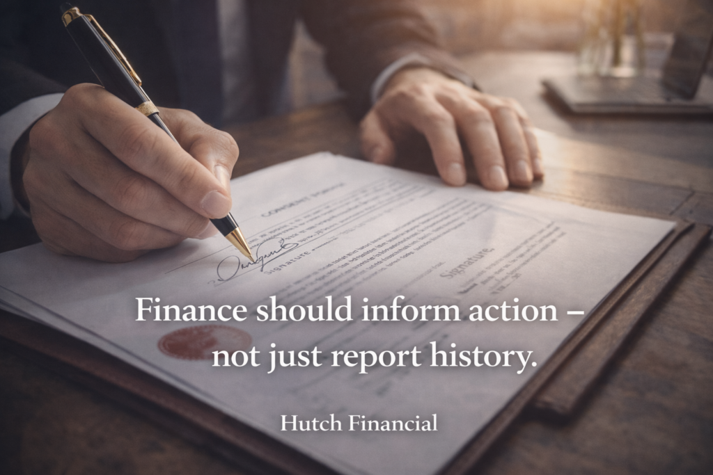 Close-up of a professional signing an official document with the overlay text “Finance should inform action — not just report history.” and Hutch Financial branding.