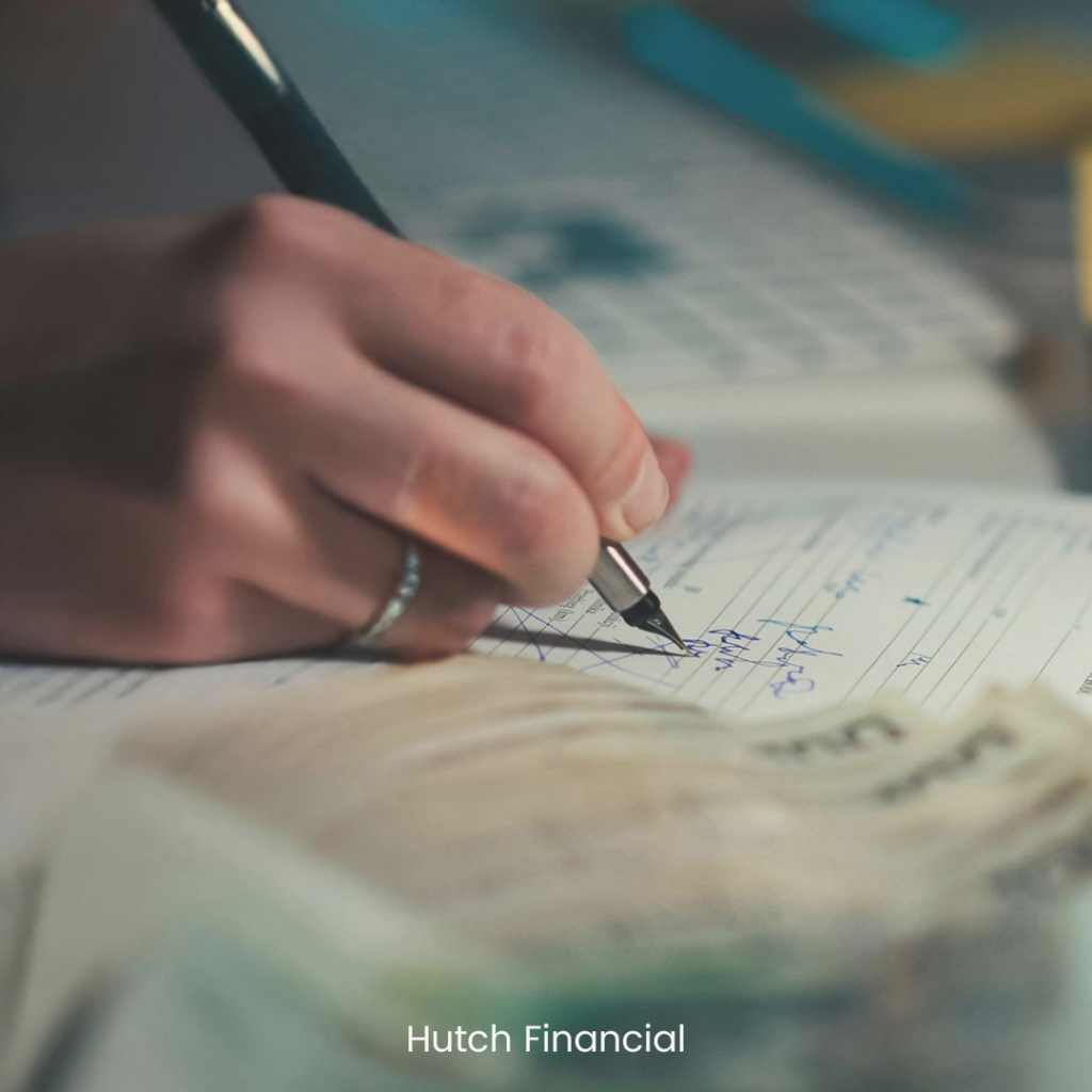 Close-up of a person writing financial notes in a notebook beside cash, representing thoughtful financial planning and leadership decision-making.